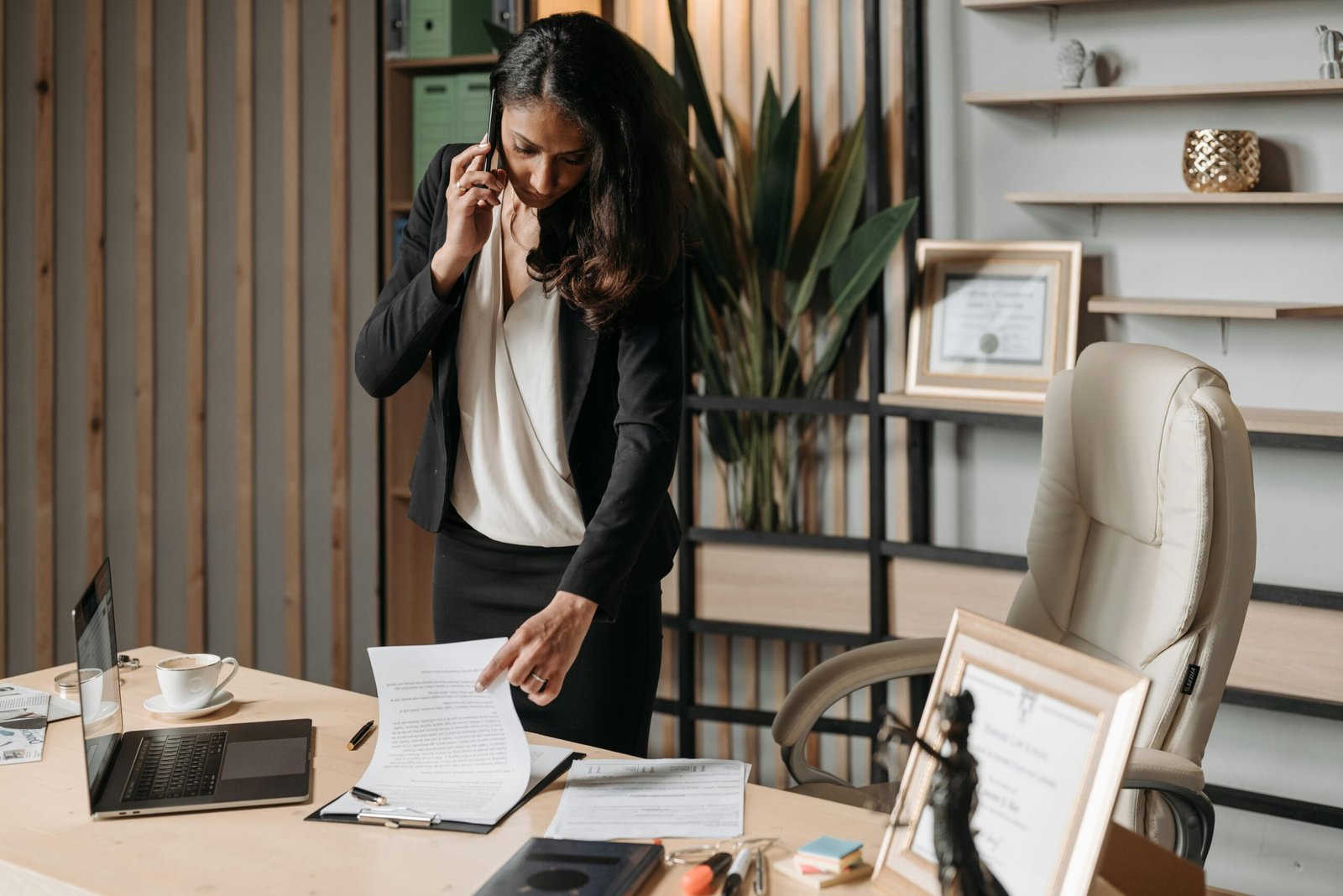 A female lawyer talking on phone while reviewing legal documents in a modern office setting.